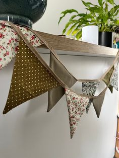 several fabric pennants hanging from a shelf in front of a potted green plant