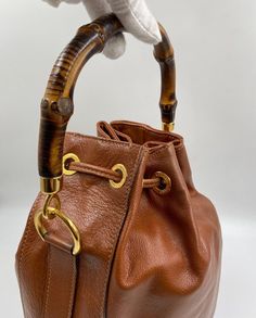 The cutest vintage brown/tan leather Gucci bucket bag with the iconic Gucci bamboo handles plus a leather crossbody strap. The crossbody strap can be taken off if you wish. This bag features gold Gucci branded hardware and gold feet on the base to protect the bag. Inside the lining is in excellent condition with a zipped interior pocket for valuables. The crossbody strap drop is 40cm. Gucci first introduced the bamboo handle in 1947 following a leather shortage as a result of the war, forcing craftspeople to experiment and look for new materials. The bamboo handles are extremely durable and a classic now for the house. This bag is in excellent vintage condition, inside the bag is immaculate., it hardly has been used. Gucci Bucket Bag, Gucci Brand, Gucci Bamboo, Bag Inside, Bamboo Handles, Timeless Handbag, Vuitton Bag, Diaper Backpack, Casual Backpack