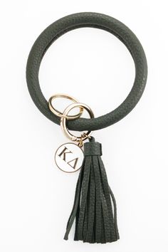 Our Sorority bangle keychains are perfect for the girl who's always got her hands full! Make your keys a new fashion accessory with this bangle keychain that can be worn on your wrist or attached to your bag. Our bangle is vegan leather wrapped with a decorative tassel and hinged clasp ring for your keys and comes with a white pendant with your sorority letters in gold print. Wrapped with vegan leather and a decorative tassel White pendant with sorority letters in gold print Hinged clasp for you