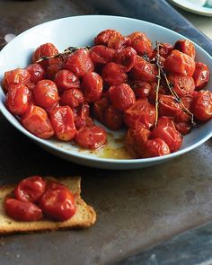 a bowl filled with tomatoes on top of a table next to crackers and a knife