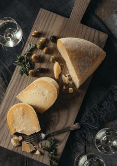 cheese and olives on a cutting board with wine glasses