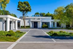 a large white house surrounded by trees and bushes in the middle of a driveway area