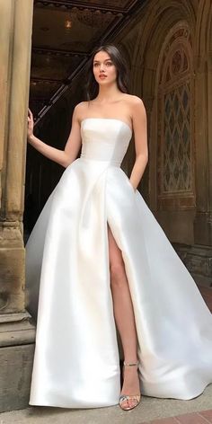 a woman standing in front of a doorway wearing a white dress with high slits