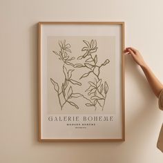 a woman holding up a framed poster with flowers on it's back and the words galerie bohemae above it