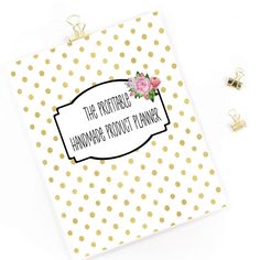 a white and gold polka dot binder with pink flowers on it, next to two tiny earrings