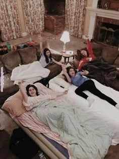 three women laying on top of a bed in a living room next to a fire place