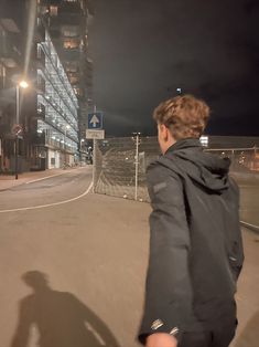 a man walking down the street in front of a tall building at night with his back turned to the camera