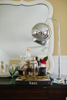 a table topped with lots of bottles and glasses on top of a wooden dresser next to a mirror