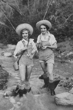 two women in cowboy hats and overalls crossing a stream with their fishing gear on