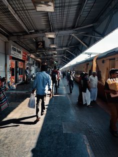 many people are walking on the sidewalk near a train station as it pulls up to the platform