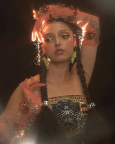 a woman with long braids wearing a headdress and holding her hands in the air