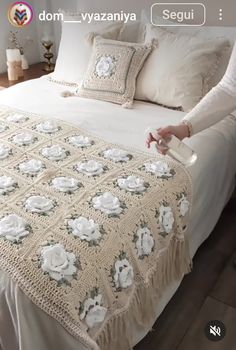 a woman standing next to a bed covered in white sheets and blankets with flowers on it