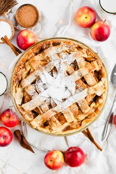 an apple pie with powdered sugar on top, surrounded by apples and cinnamon sticks