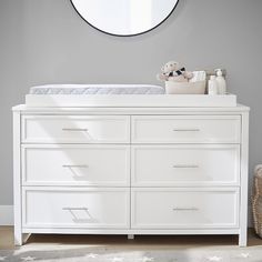 a baby crib with a teddy bear on it and a round mirror above it