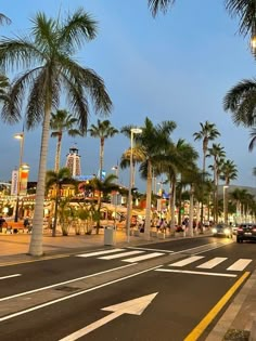 palm trees line the street in front of shops and restaurants at dusk with people walking on the sidewalk