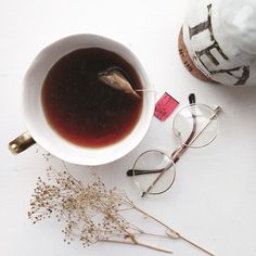 a cup of tea next to a pair of reading glasses on a table with dried flowers