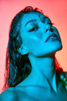 a woman with wet hair and blue eyes posing in front of a red background, her head tilted to the side