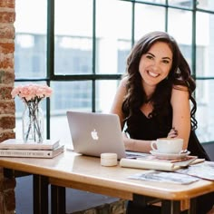 a woman sitting at a table with a laptop and coffee in front of her smiling