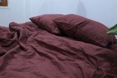 an unmade bed with red sheets and pillows on top of it, next to a plant