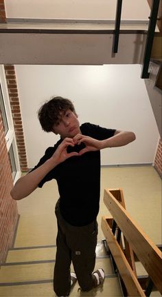 a young man making a heart shape with his hands while standing in front of stairs