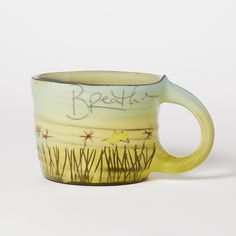 a yellow and white coffee cup with writing on the side that says breathe in grass