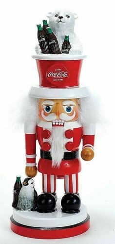 a coca - cola nutcracker with two cats on it's head and one cat in its mouth