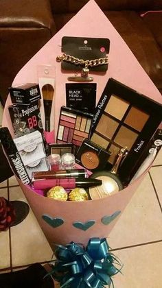 a pink gift box filled with makeup and other items on a tile floor next to a brown couch