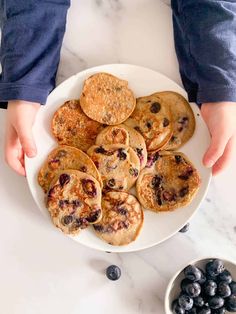 blueberry pancakes on a white plate with hands grabbing one