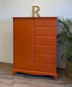 an orange dresser with the letter r on it's top and bottom drawer, next to a potted plant