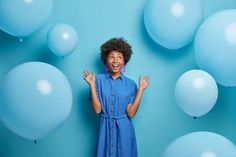 a woman standing in front of balloons with her hands up to the side and smiling