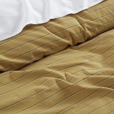 an unmade bed with white sheets and brown striped comforter on top of it