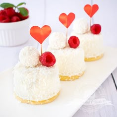 three small cakes on a white plate topped with raspberries and strawberries in the shape of hearts