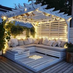 an outdoor seating area is lit up with string lights and white pillows on the couch