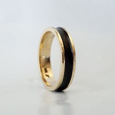 a ring with black and gold inlays sits on a white surface, ready to be worn