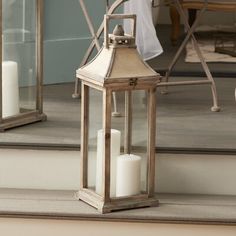 a lantern with two candles on the ground in front of a mirror that is outside