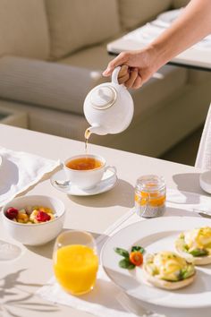 a person pouring tea on top of a table with plates and bowls filled with food