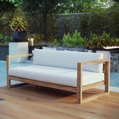 a white couch sitting on top of a wooden floor next to a swimming pool with trees in the background