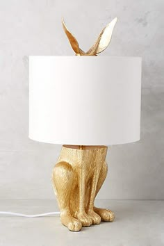 a golden cat lamp with a white shade on it's head and tail sitting next to a gray wall