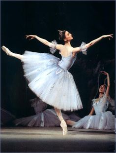 two ballerinas in white tutus and blue dresses, one with her arms outstretched