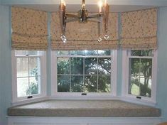 a window seat in front of two windows with roman shades on the top and bottom