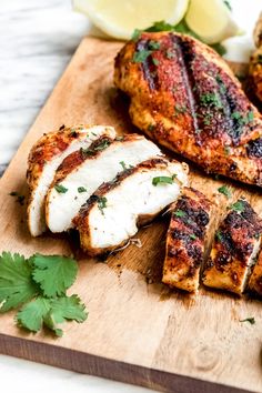 grilled chicken on a cutting board with parsley and lemon wedges next to it