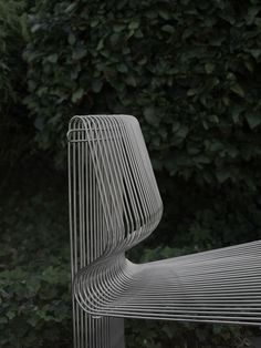 a close up of a metal bench near some bushes and trees in the back ground