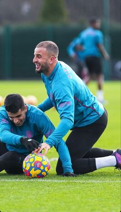 two soccer players in blue shirts and black pants are on the grass with a ball