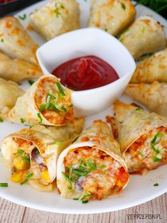 a white plate topped with vegetable spring rolls next to a bowl of ketchup