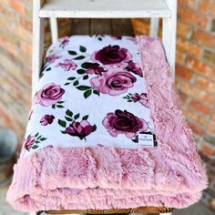 a white chair with pink flowers on it and a blanket over the seat area in front of a brick wall