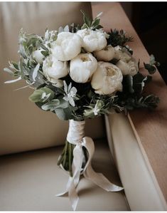 a bridal bouquet with white flowers and greenery on the side of a couch