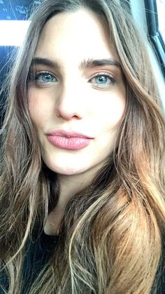 a woman with long hair and blue eyes is sitting in a car looking at the camera