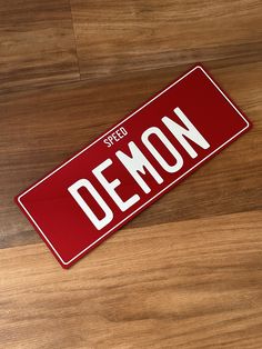 a red and white sign that says demon on the side of a wooden floor with wood grain