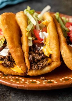 three tacos on a plate with lettuce, tomatoes and other toppings