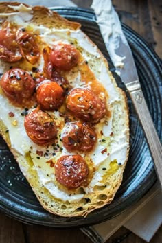 a piece of bread topped with tomatoes and cheese on top of a black plate next to a fork